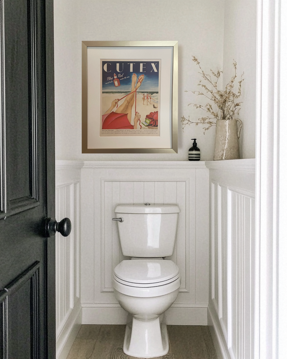 Framed 1946 Cutex Play Red vintage beauty advertisement displayed above a toilet in a bright powder room