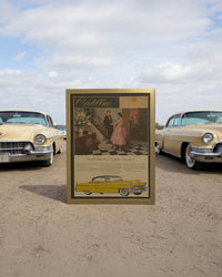 Original 1950s Cadillac magazine advertisement framed in gold, featuring an elegant couple and classic yellow Cadillac