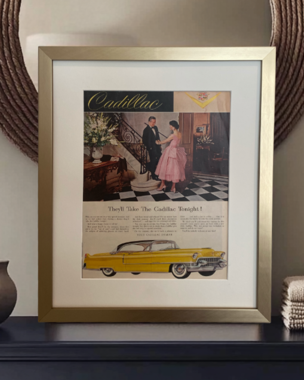 Original Cadillac “They’ll Take the Cadillac Tonight” vintage advertisement in a brushed brass frame with an off-white mat, styled on a dark dresser.