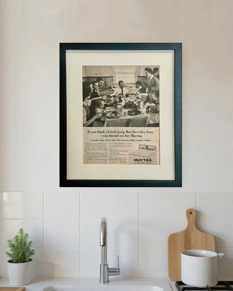 Framed original 1965 Maytag advertisement displayed above a kitchen sink in a bright neutral kitchen