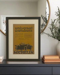 Original Michelin “Universal Usefulness” vintage magazine advertisement displayed in a black frame on a styled entryway console with a round brass mirror and neutral décor.