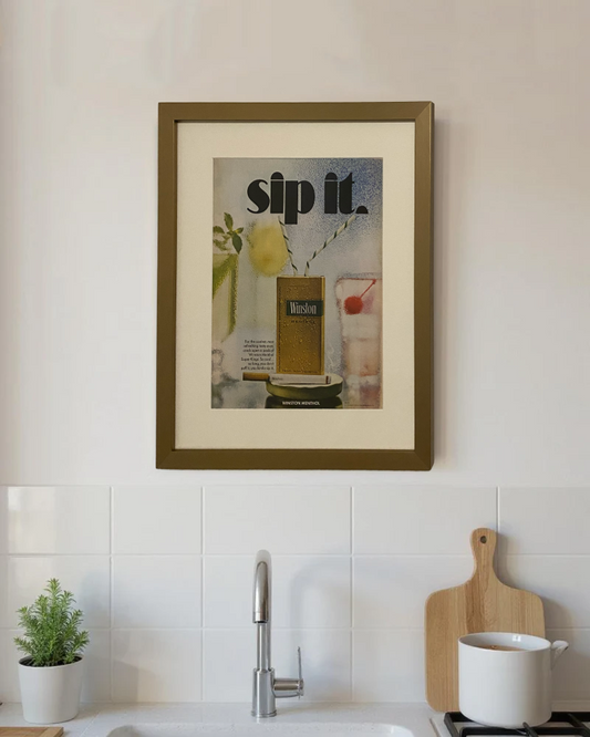 Original Winston Menthol “Sip It.” vintage cigarette advertisement framed in a thin brass frame displayed on a modern kitchen wall.
