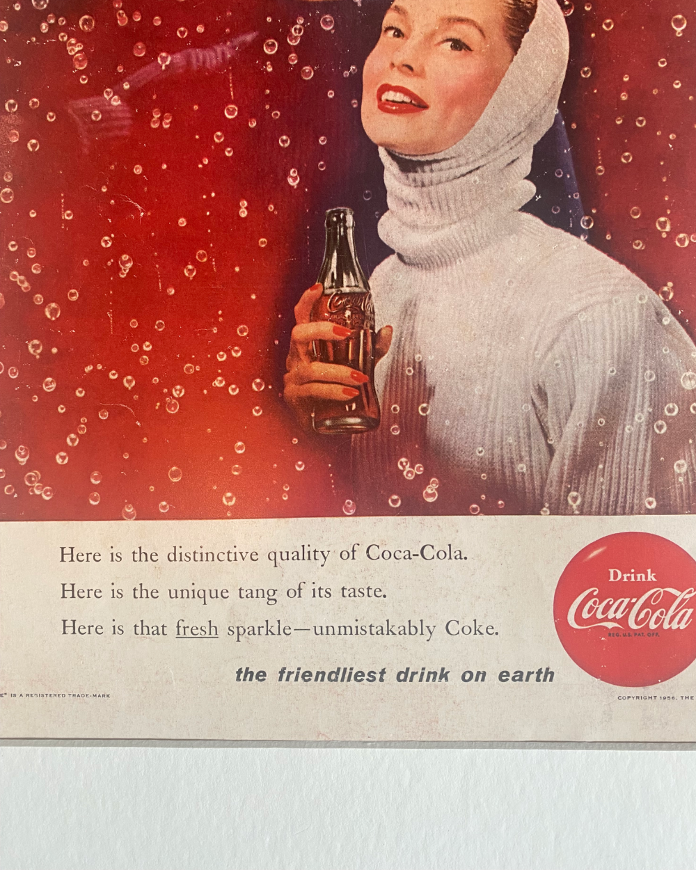 Close-up of an original vintage Coca-Cola advertisement showing the classic glass bottle, sparkling bubbles and period typography